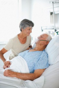 Wife watching husband with oxygen mask in hospital bed